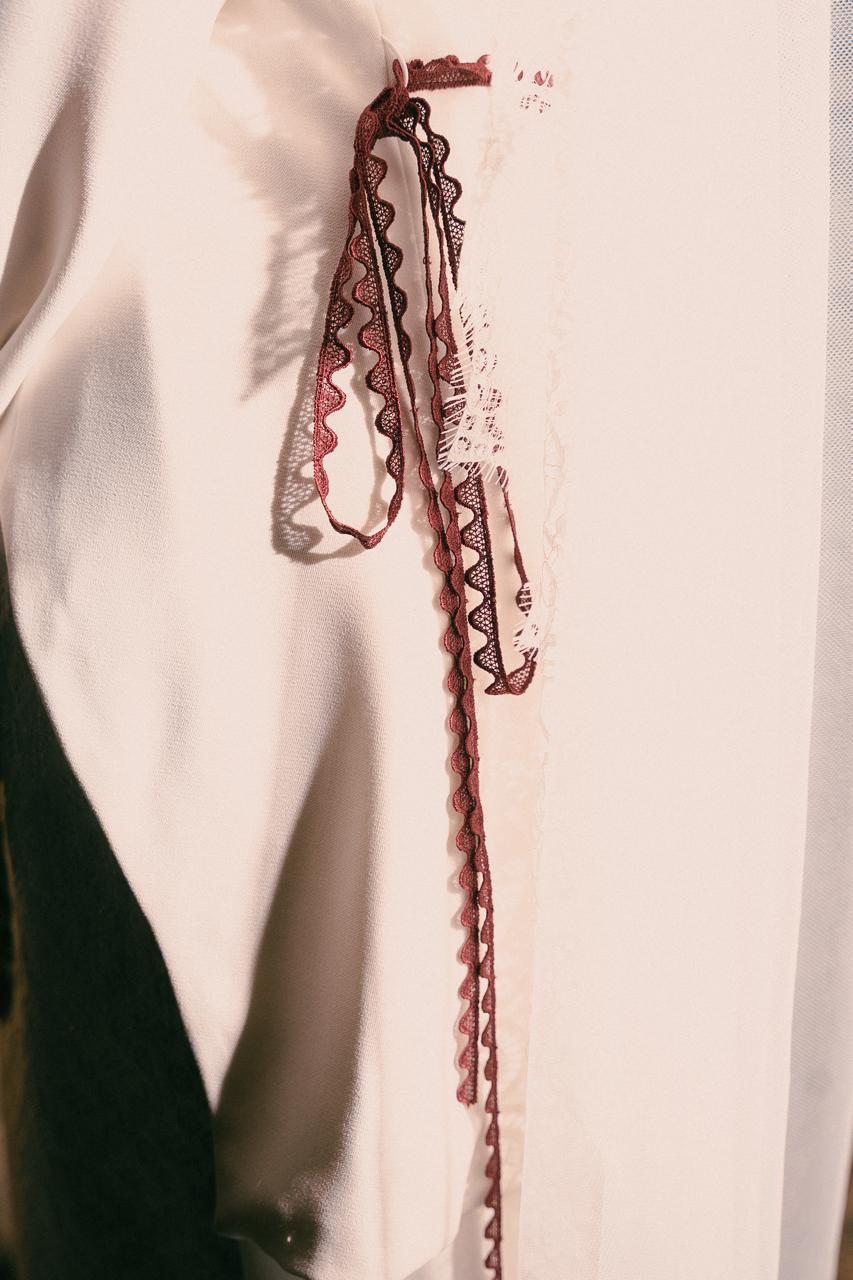 A close-up of maroon lace trim on the collar of a cream kebaya.