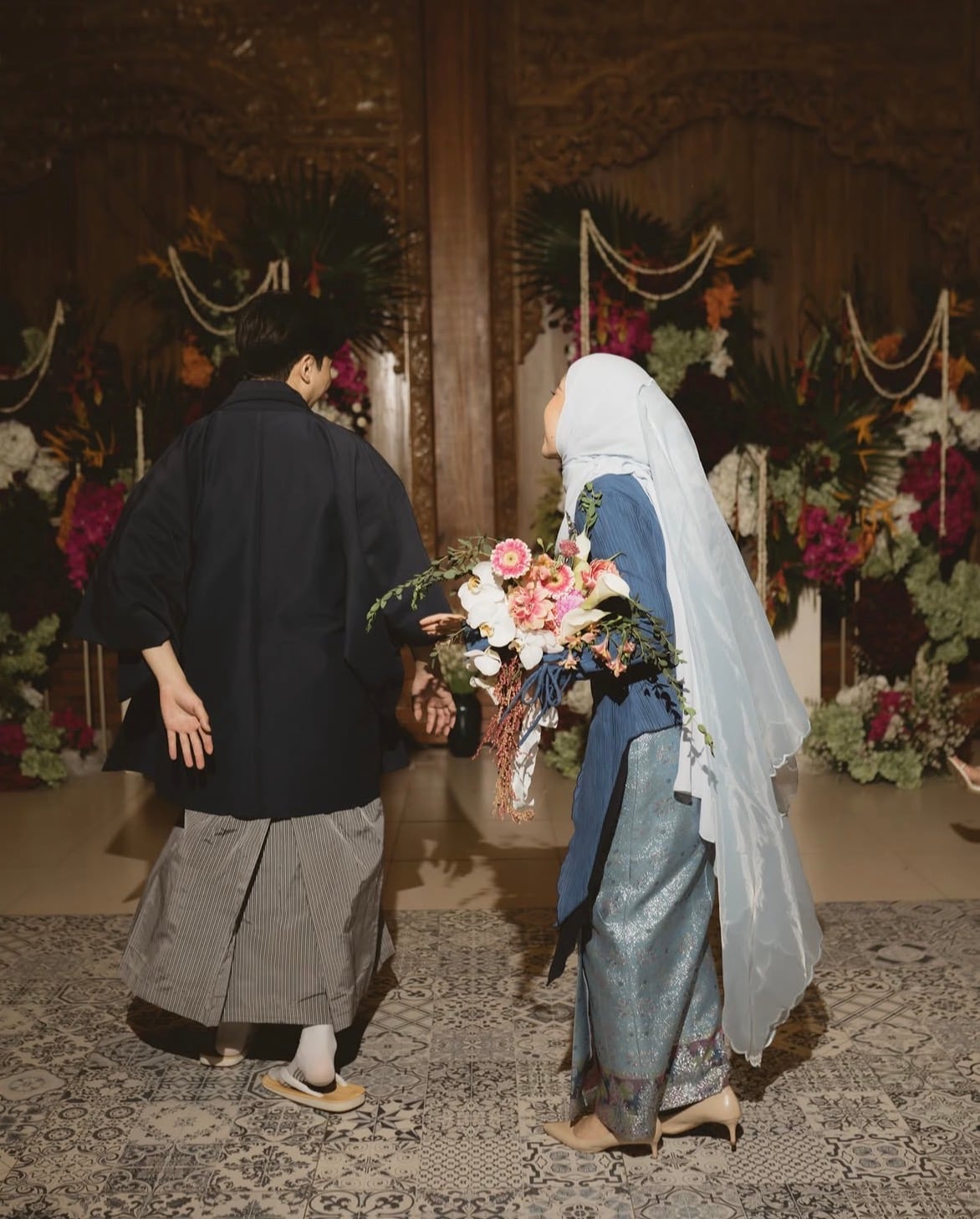A couple walking in together, framed by flowers at the ceremony.