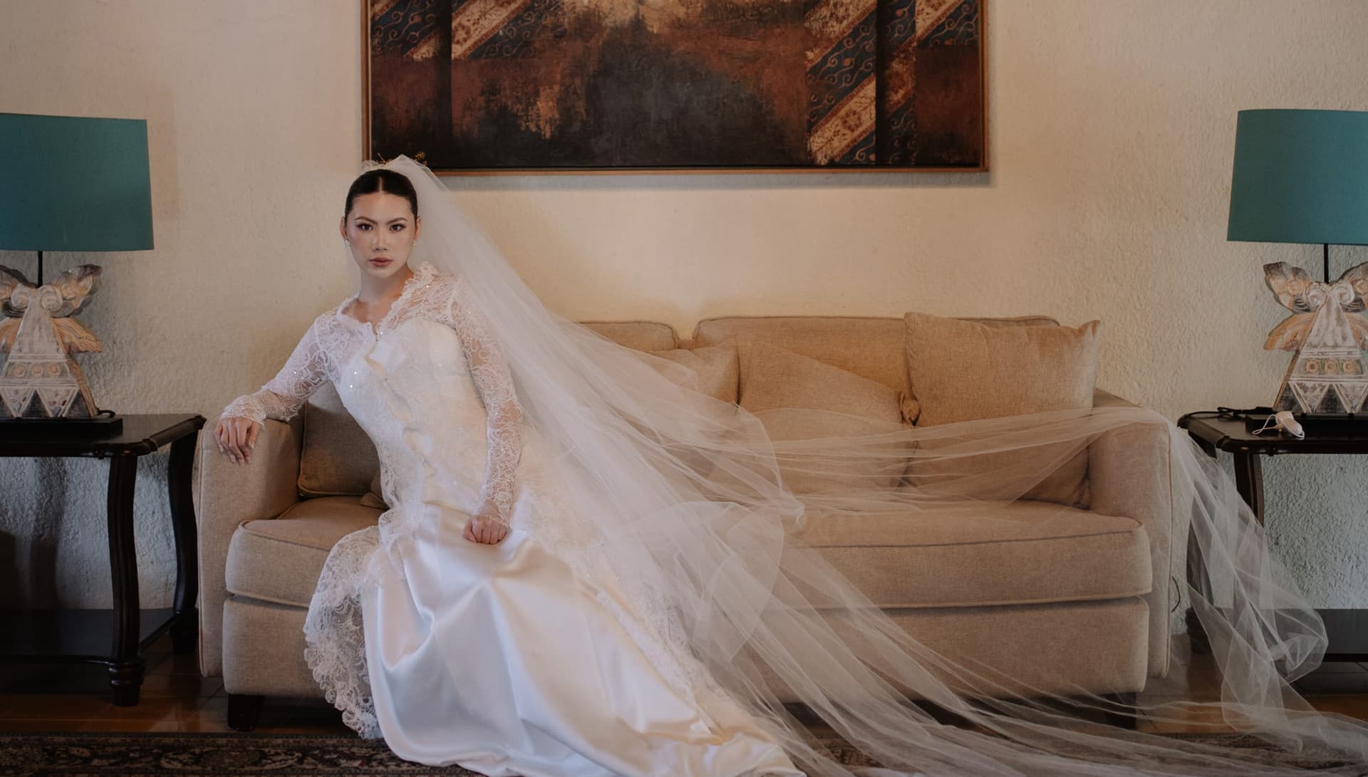 Pengantin perempuan bergaun lace duduk di bawah karya seni besar sebelum upacara.